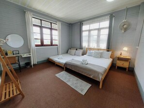 Ein Schlafzimmer mit zwei Betten, einem Schreibtisch, einem Stuhl, einem Nachttisch mit Lampe und einem großen Fenster.
