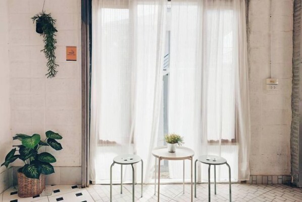 A room with a large window, two stools, a small table with a plant, and a hanging plant on the wall. - The Warehouse - Ayutthaya (Ayutthaya)