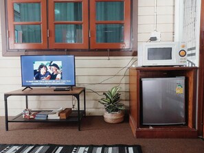 A room with a television on a stand, a small refrigerator, a potted plant, and a window with curtains. - The Warehouse - Ayutthaya (Ayutthaya)