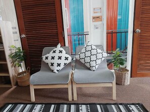 Two grey chairs with patterned cushions, a woven rug, and a wooden door with a sign indicating quiet hours. - The Warehouse - Ayutthaya (Ayutthaya)