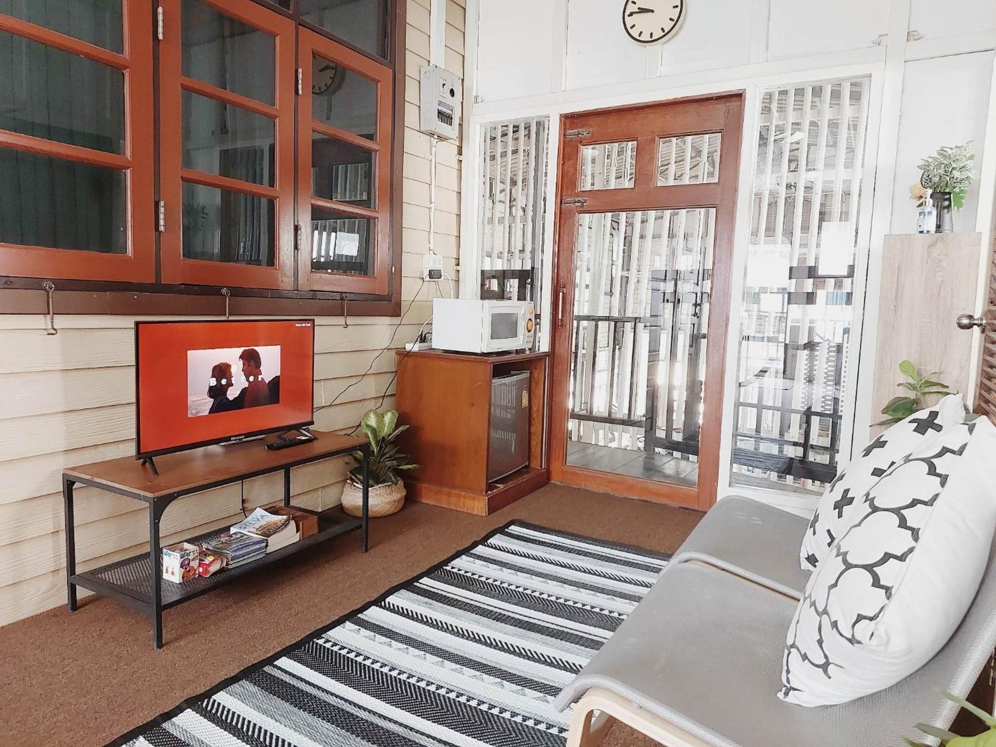 Een woonkamer met een televisie, een bank, een kamerkleed met dessin en een raam met gordijnen.