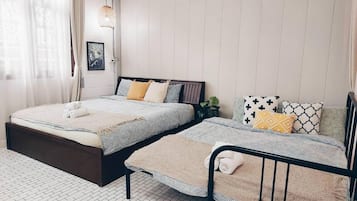 Un dormitorio con dos camas, una ventana con cortinas translúcidas, una lámpara colgante y un cuadro en la pared.