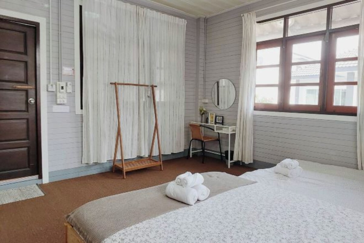 Habitación de hotel con cama, escritorio, silla, lámpara colgante y ventana con cortinas.