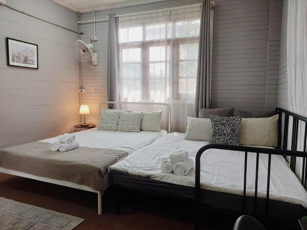 A double bed with a metal frame, a bedside table with a lamp, and a window with curtains. - The Warehouse - Ayutthaya (Ayutthaya)