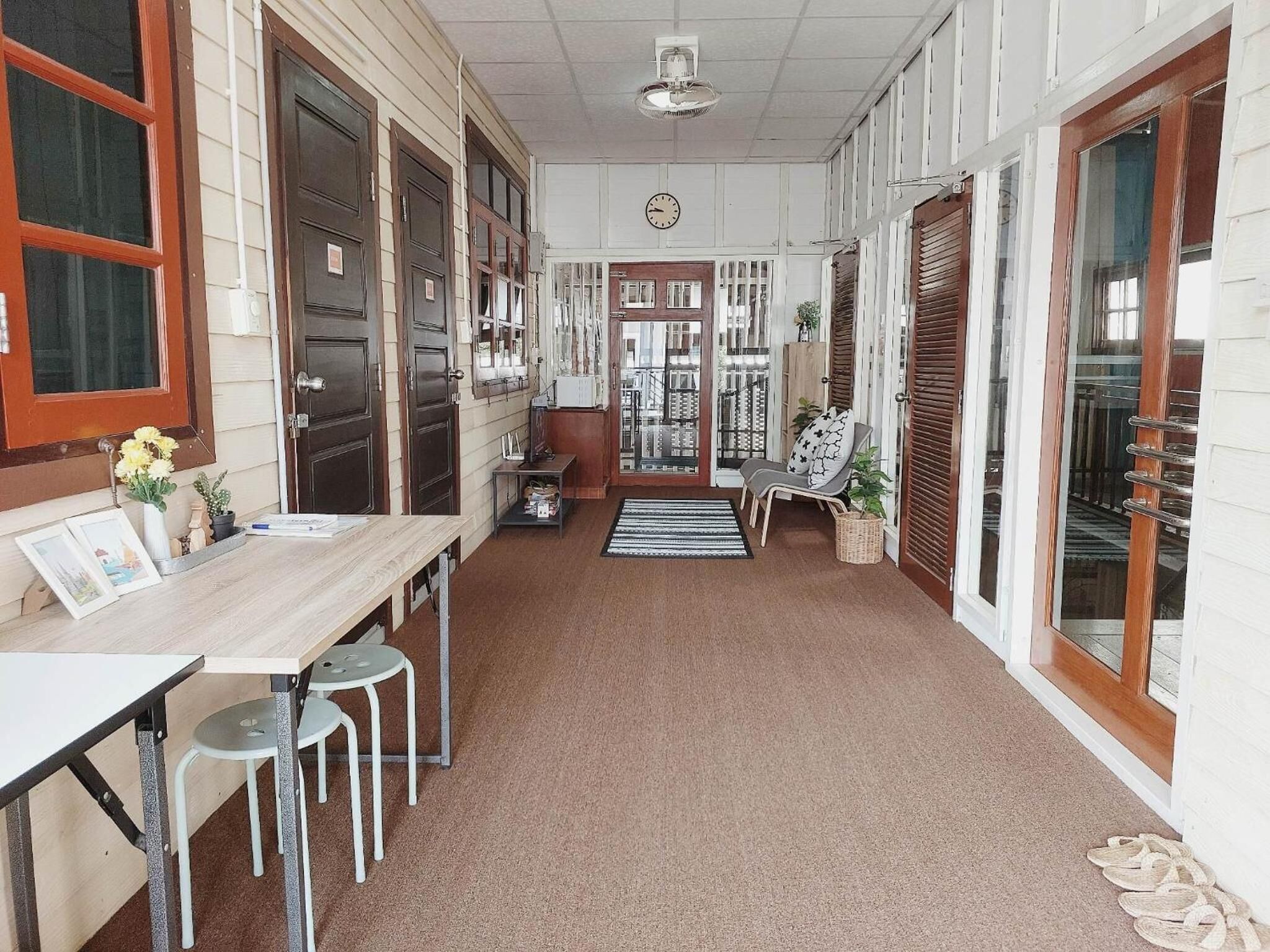 Um corredor com uma mesa de madeira, cadeiras, um relógio e uma porta que dá para outro quarto.