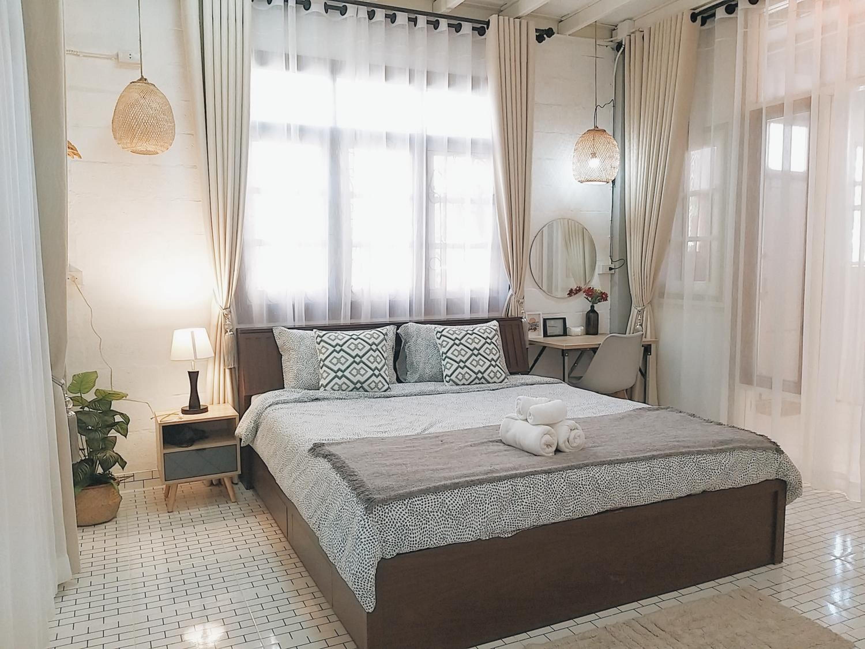 A hotel room with a large bed, a bedside table, a lamp, a mirror, and a potted plant.