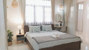 A hotel room with a large bed, a bedside table, a lamp, a mirror, and a potted plant.