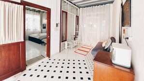 A hotel room with a bed, a desk, a chair, a radiator, and a window with curtains. - The Warehouse - Ayutthaya (Ayutthaya)