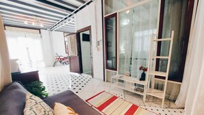 A modern living room with a sofa, a coffee table, and a patterned rug. There is a sliding glass door leading to a balcony with a motorcycle parked outside. - The Warehouse - Ayutthaya (Ayutthaya)