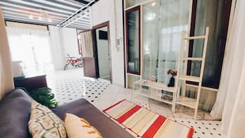 A modern living room with a sofa, a coffee table, and a patterned rug. There is a sliding glass door leading to a balcony with a motorcycle parked outside.