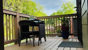 A wooden deck with a table and chairs, a potted plant, and a view of trees and a building in the background.