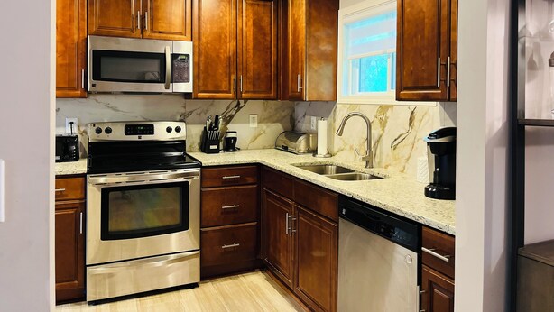 A modern kitchen with wooden cabinets, stainless steel appliances, a marble countertop, and a built-in dishwasher.