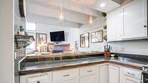 Une cuisine moderne avec des meubles blancs, un plan de travail en granit et des luminaires suspendus.