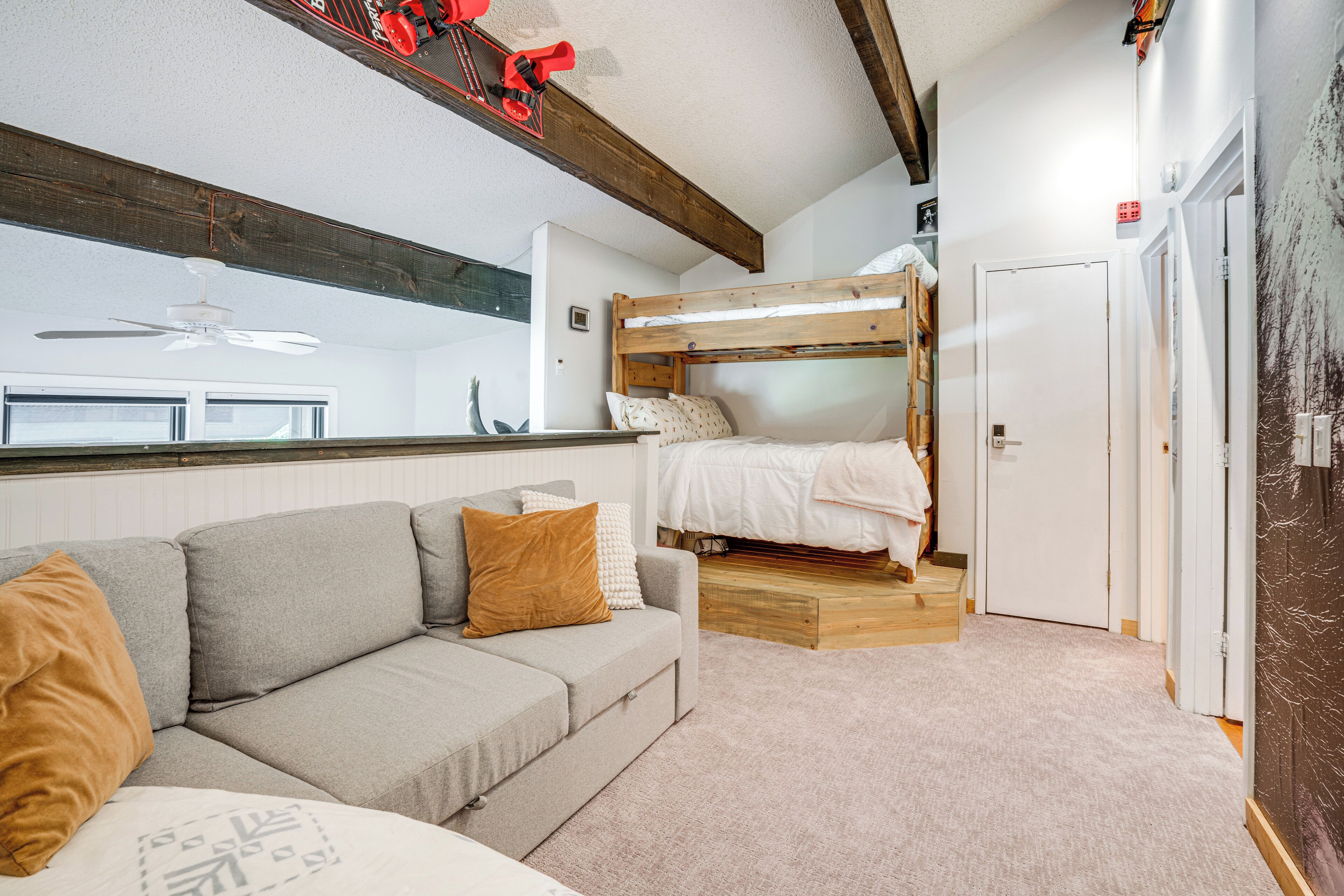 A compact room with a bunk bed, a sofa, a ceiling fan, and a door.