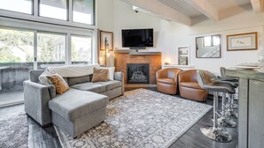 Un salon chaleureux avec une cheminée, un canapé, une table basse et un téléviseur fixé au mur.
