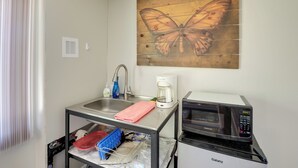 Una kitchenette con un lavamanos, un microondas, una cafetera y una repisa con vajilla.