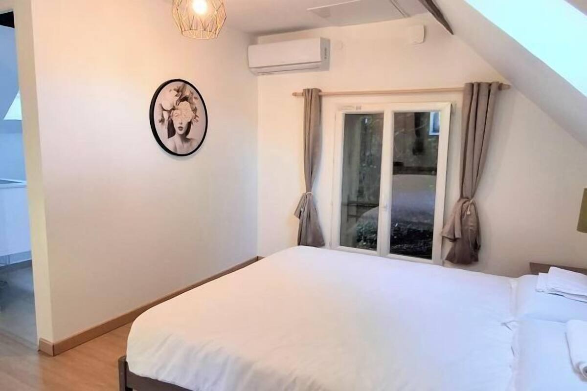 Een slaapkamer met een groot bed, een raam met gordijnen, een airconditioning en een aan de muur bevestigd schilderij.