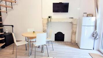 Un comedor con mesa y sillas, una chimenea, un televisor montado en la pared y un refrigerador.