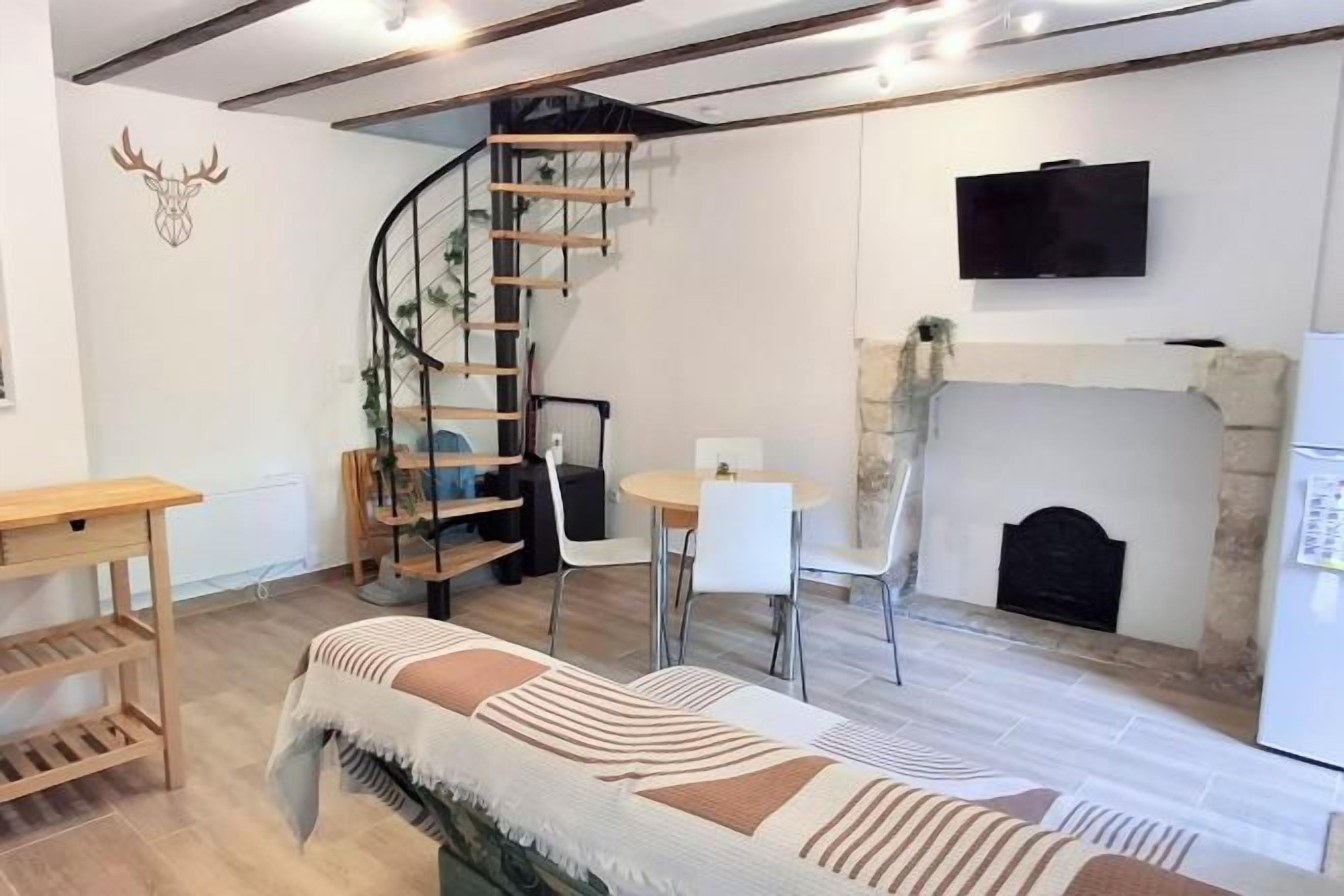 Una sala de estar acogedora con una escalera en espiral, una chimenea, un televisor montado en la pared y una cama con manta a rayas.