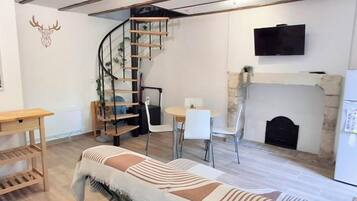 Una sala de estar acogedora con una escalera en espiral, una chimenea, un televisor montado en la pared y una cama con manta a rayas.