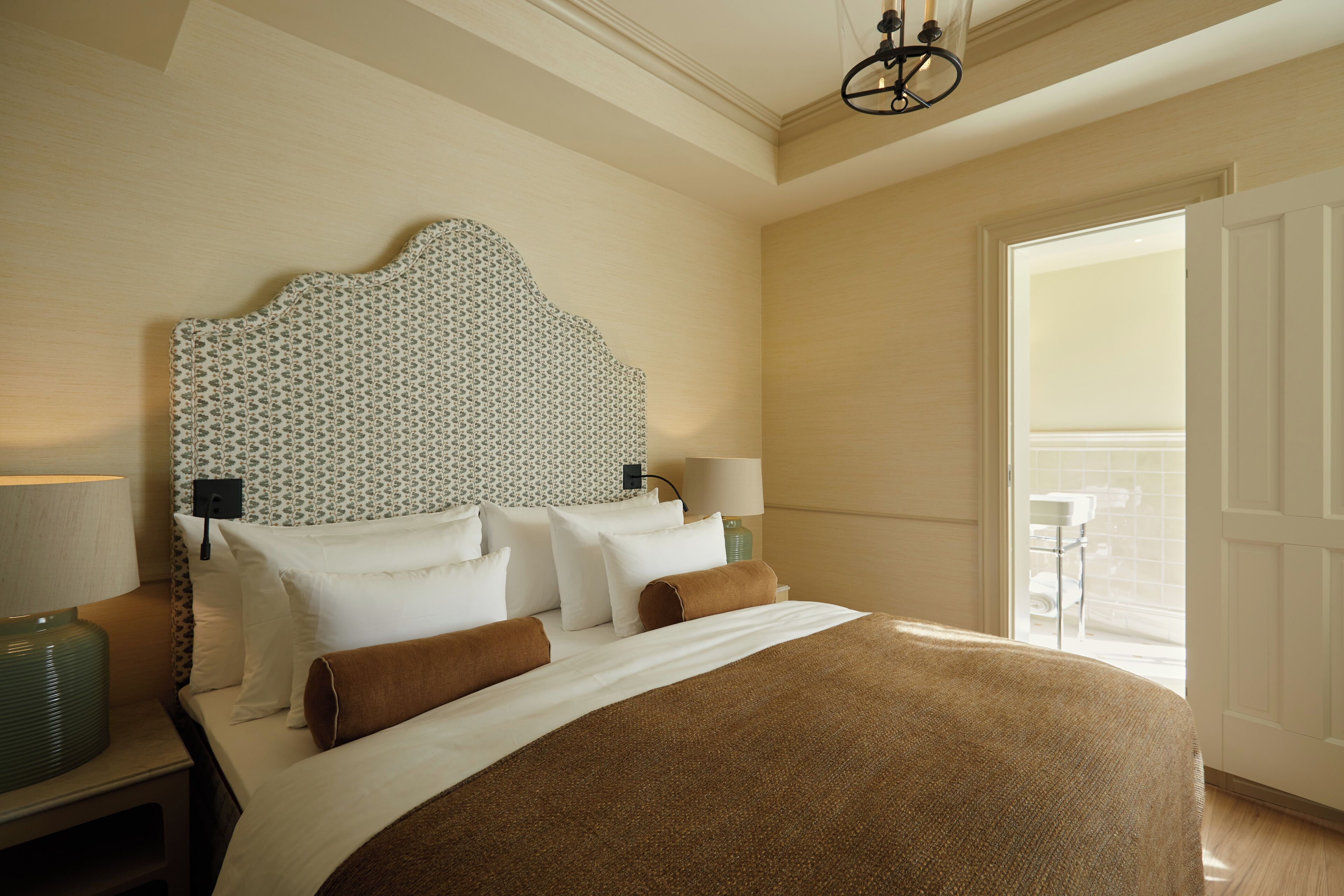 A hotel room with a large bed, a patterned headboard, bedside lamps, and a view of the outdoors.