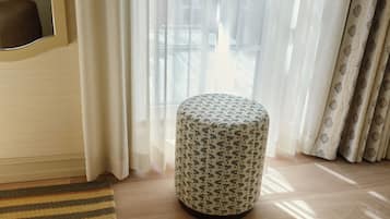 Una habitación con un otoman redondo, un tapete a rayas y cortinas traslúcidas.
