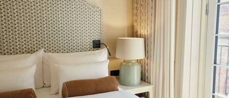 A hotel room with a bed, pillows, a lamp, and a window with curtains.