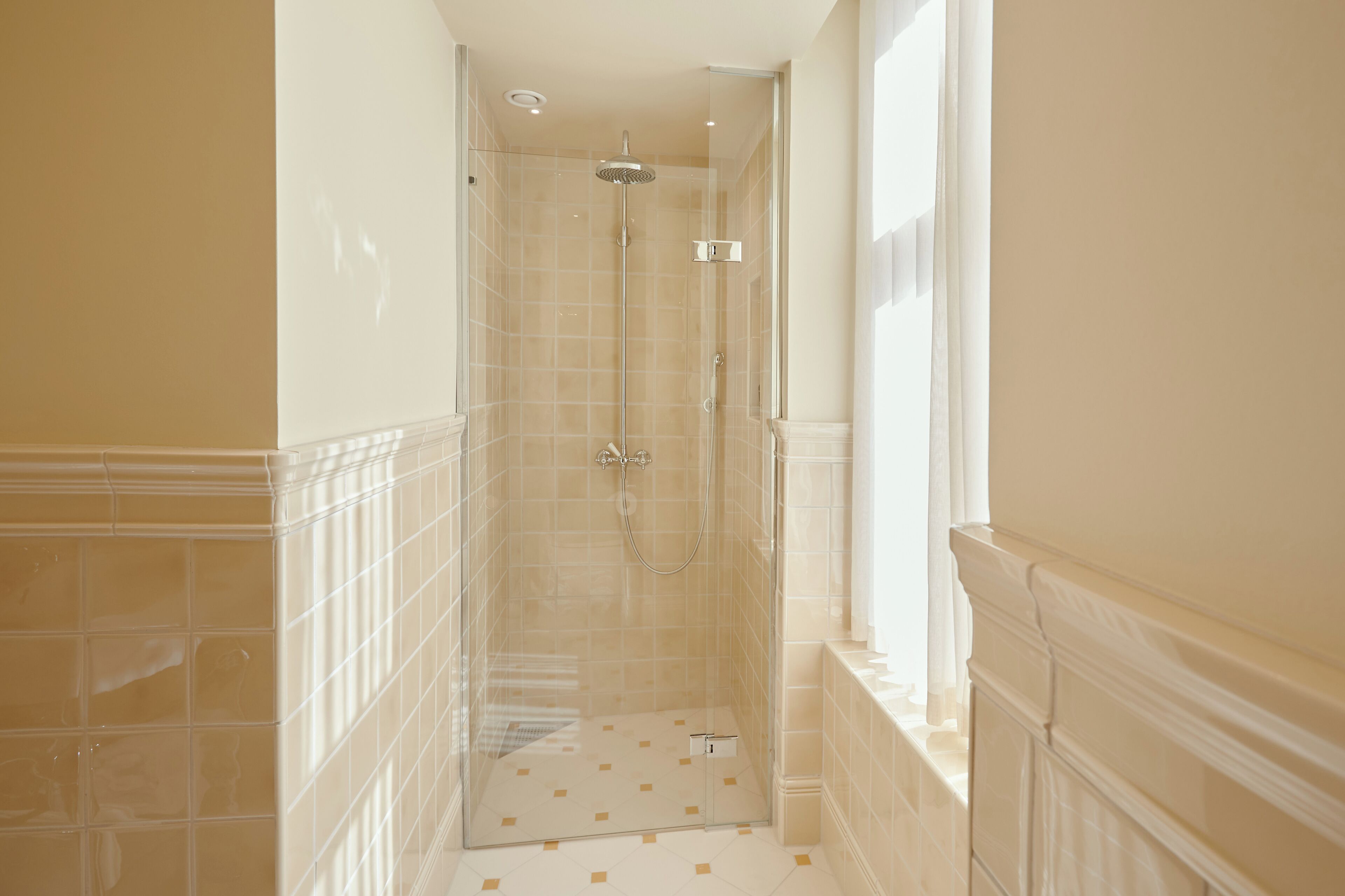 A narrow, tiled shower area with a glass door, a showerhead, and a control panel.