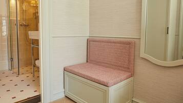 A corner bathroom with a shower, a sink, and a bench.