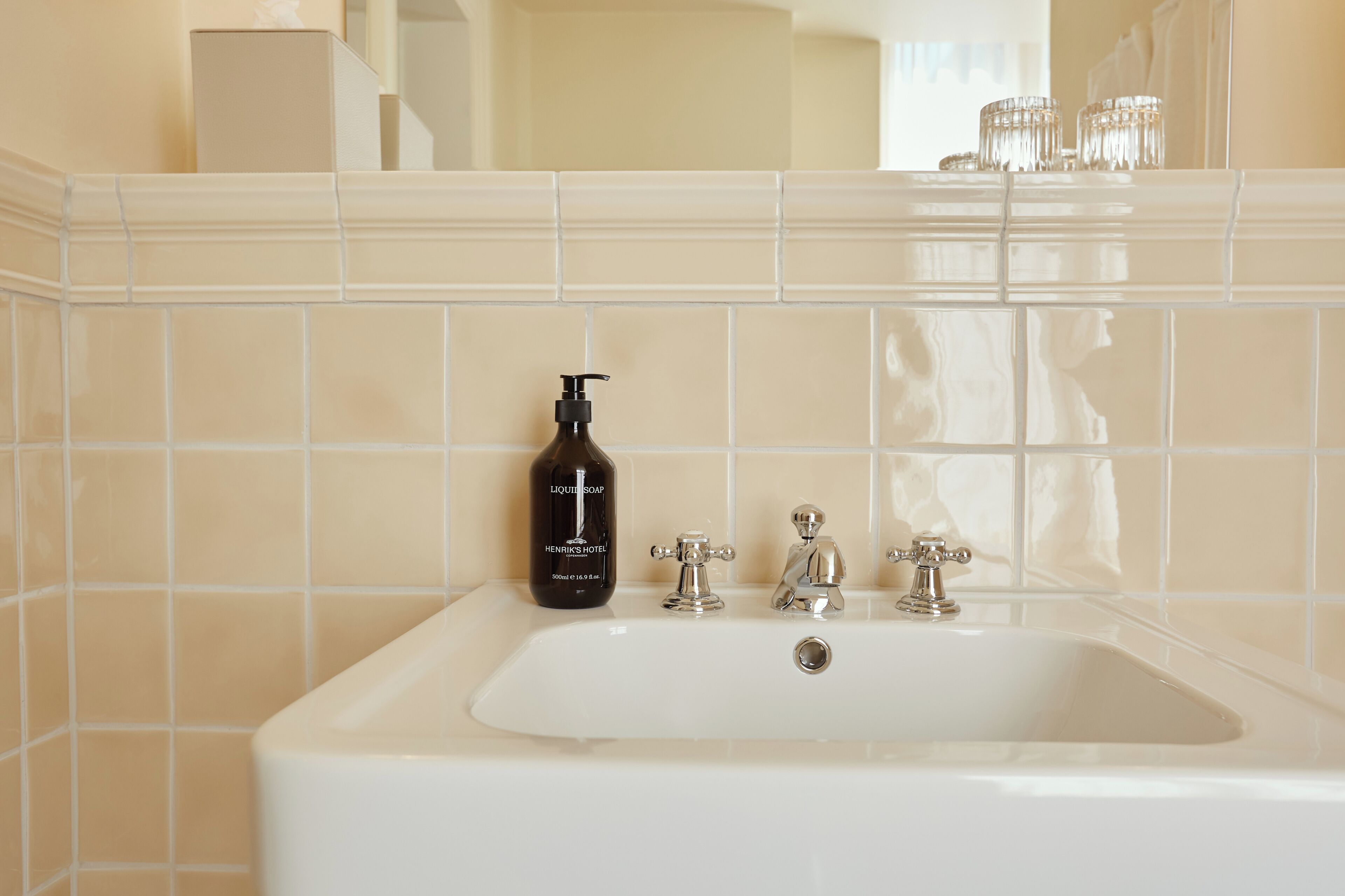 A bathroom with a white sink, two faucets, and a bottle of liquid soap.