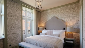 A neatly arranged bedroom with a large bed, bedside lamps, a bench, and a view through a window. -  Henrik's Hotel (Copenhagen)
