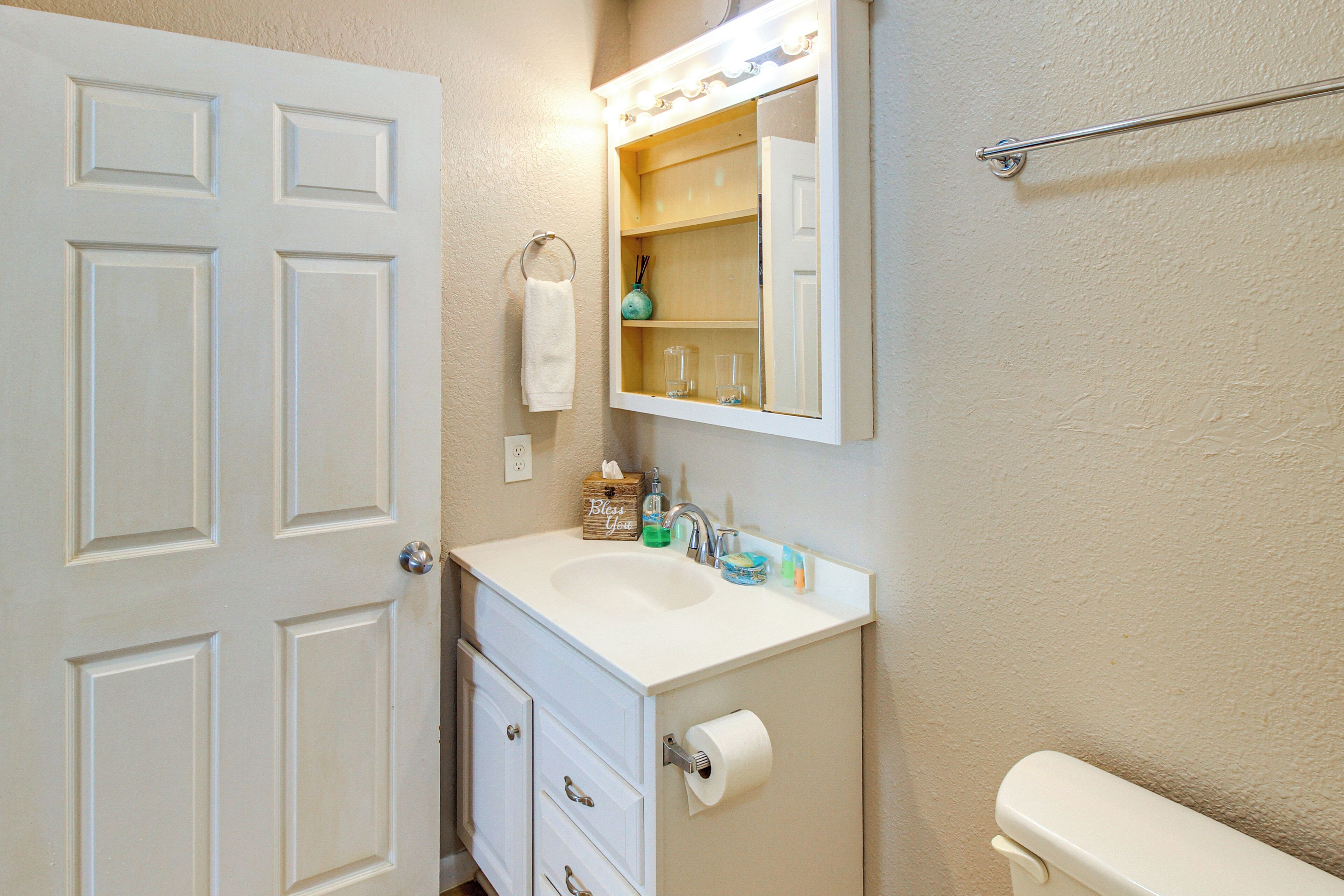 A bathroom with a white sink, mirror, and toilet. There is a towel hanging on the wall and a bottle of hand soap on the sink.