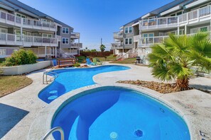 A swimming pool with a wooden deck, surrounded by a fence and palm trees. - Steps to Shore: Condo w/ Balcony in Port Aransas (Port Aransas)