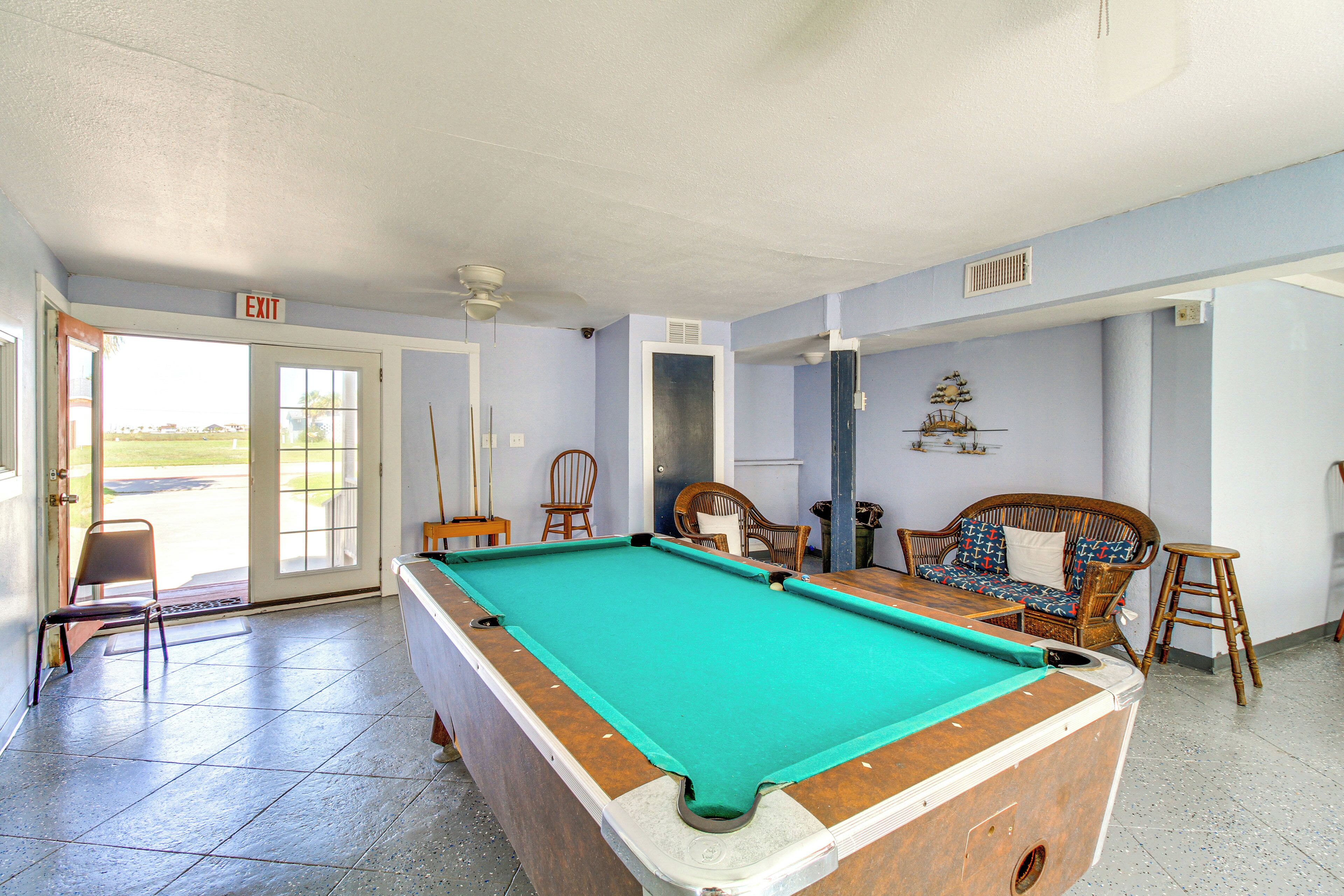 A pool table in a room with a door leading outside, a wicker sofa, and a chair.