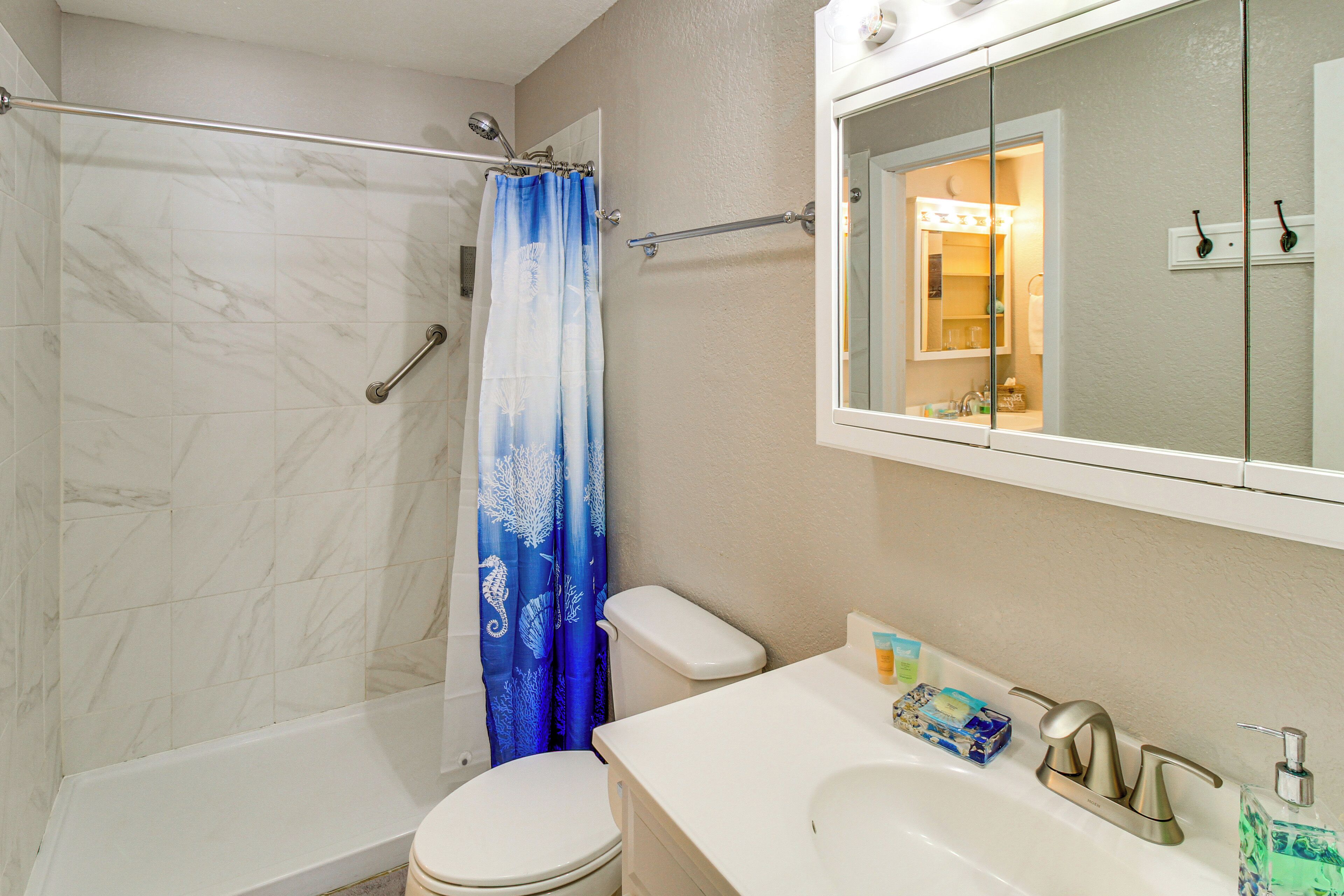 A bathroom with a shower, toilet, sink, and mirror.