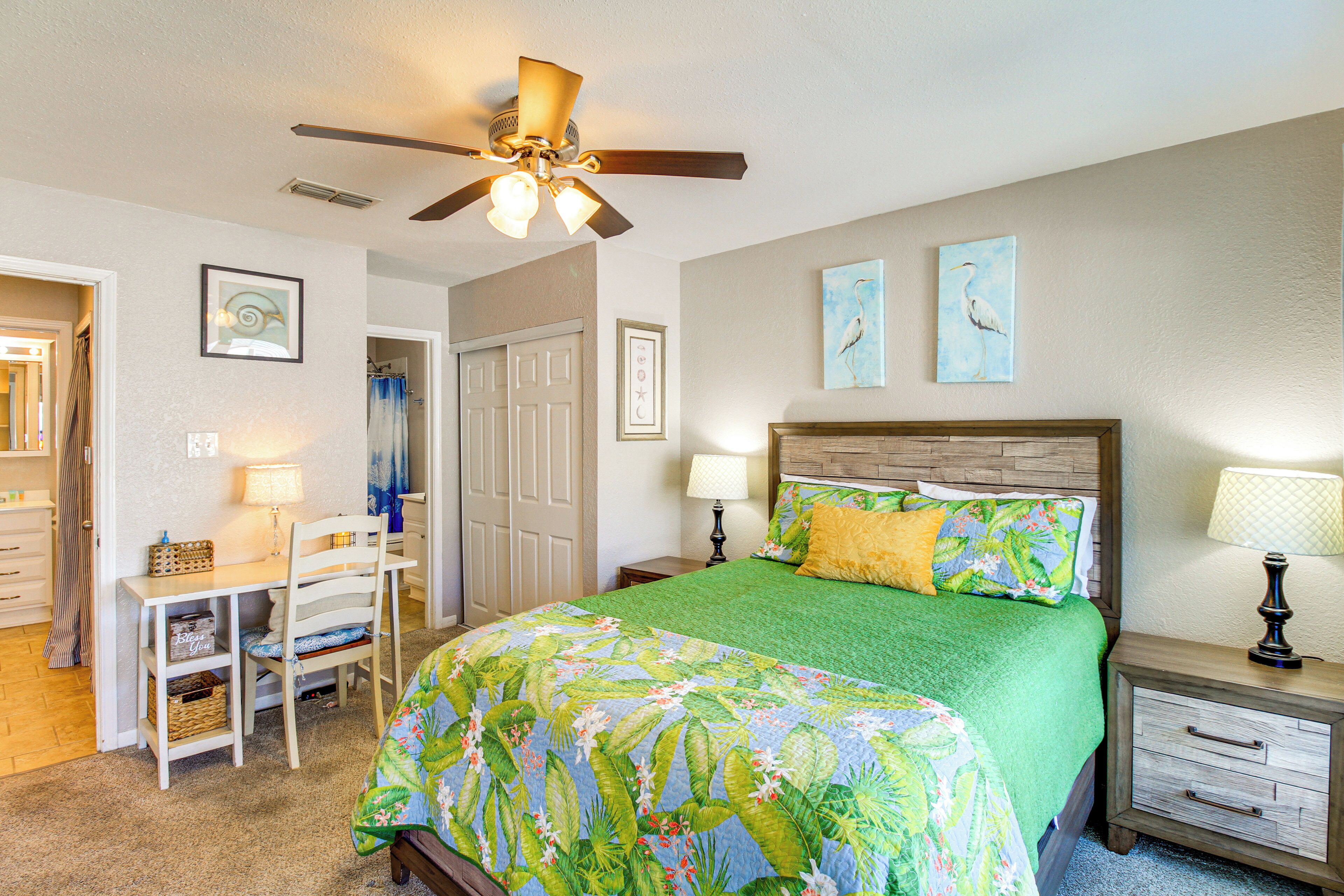 A bedroom with a bed, a desk, a chair, a nightstand, and a ceiling fan.