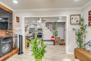 A modern living room with a fireplace, a ceiling fan, and a staircase leading to the kitchen.