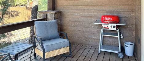A wooden deck with a wicker chair and a barbecue grill.