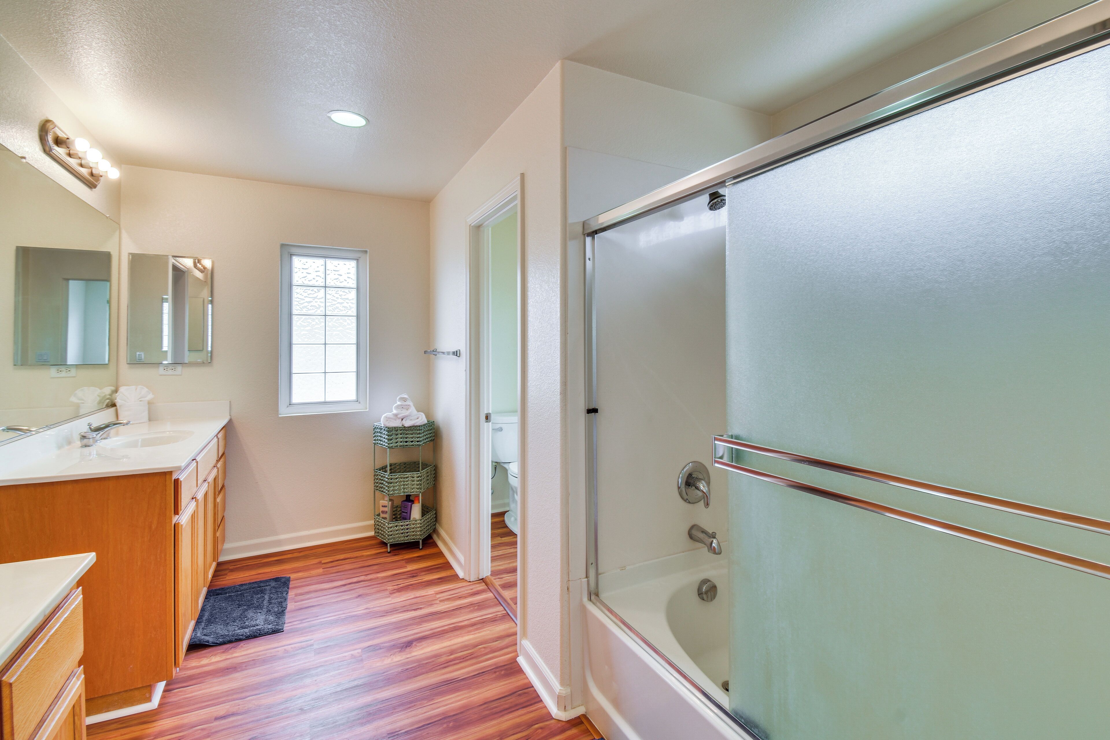 Une salle de bain avec une douche à parois de verre, des meubles en bois, un lavabo et une fenêtre.