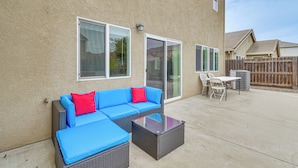 An outdoor patio with a blue sectional sofa, a glass-top coffee table, and a white table and chairs.