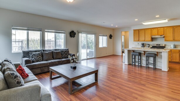 A spacious living room with a sofa, coffee table, and a kitchen area with wooden cabinets and a bar stool.