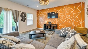 Una sala de estar con un sofá modular, una mesa de centro, un televisor montado en la pared y una pared decorativa con motivos geométricos.