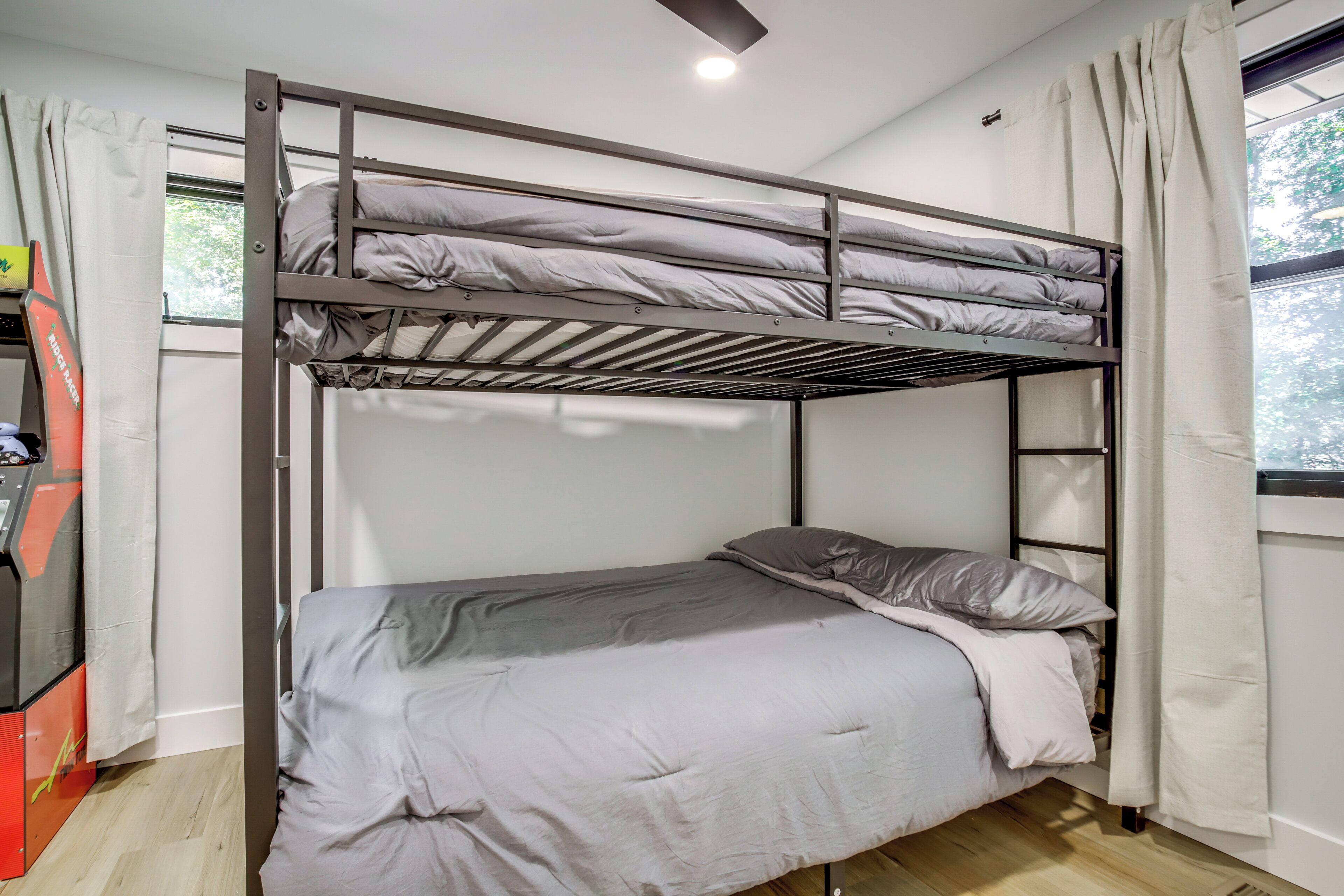 A bunk bed with a lower bed and a top bunk, a ceiling fan, and a window with curtains.