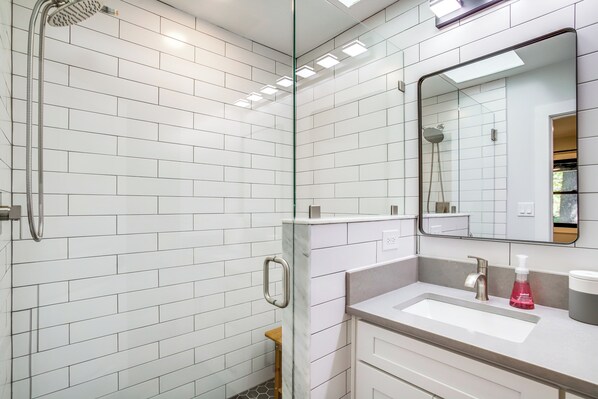 A modern bathroom with white subway tiles, a glass shower enclosure, a vanity with a sink, and a mirror. - 2 1/2 Mi to Bethany Boardwalk! Private Retreat! (Ocean View)