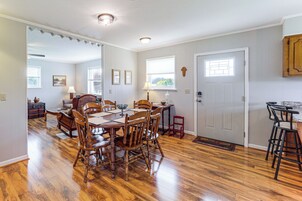 Un comedor con una mesa y sillas de madera, una cocina con mostrador y taburetes de madera, y una puerta con ventanal.
