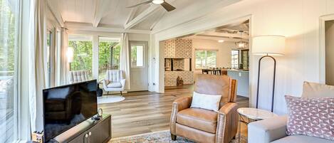 A spacious living room with a large flat-screen TV, leather armchair, and a sofa.