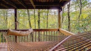 Un hamac sur une terrasse en bois, avec vue sur une forêt.