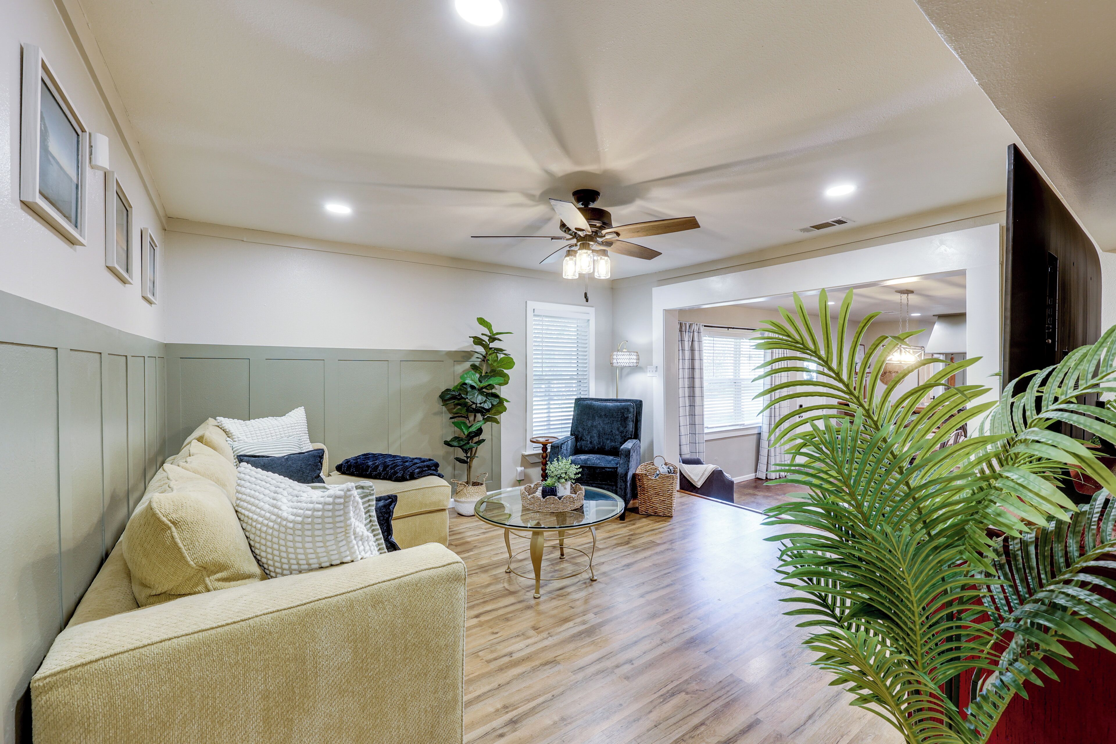 A living room with a sofa, armchair, coffee table, and potted plants.