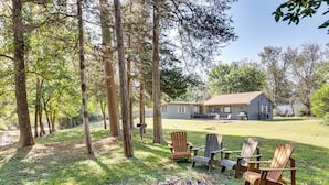 Une maison avec un jardin, trois chaises Adirondack et un foyer extérieur.