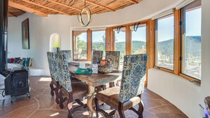 A dining area with a wooden table, patterned chairs, and a view of the outdoors through large windows. - Panoramic Vistas: Glorieta Adobe Near Pecos River (Glorieta)